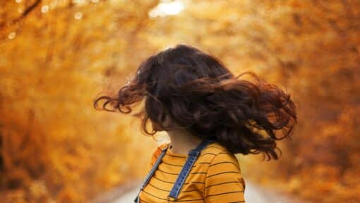 Femme aux cheveux bruns en mouvement sur une route bordée d'arbres d'automne